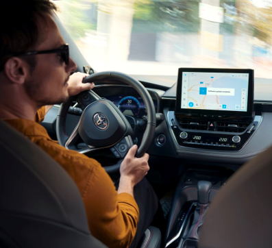 Muž v oranžovém svetru za volantem Toyoty odbočuje doprava. Na multimediálním systému ve vozidle se zobrazuje aktualizace softwaru.